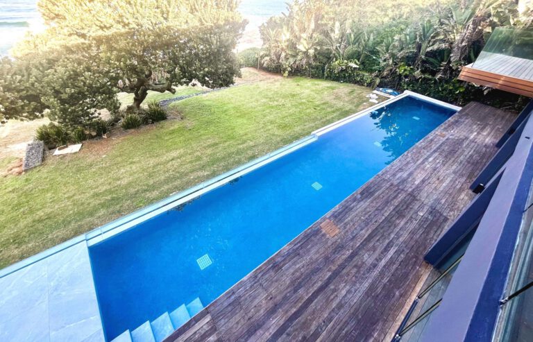 A dark-water lane edged in timber decking beneath an established tree, built by Kenny Matthews Pools cc, NSPI Bronze 2025